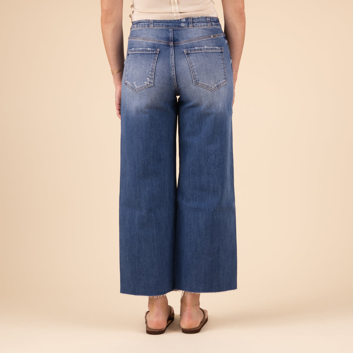 Back view of the jeans featuring classic back pockets, a fitted high-rise waist, and wide legs with frayed hems. The model stands facing away, with her arms at her sides.