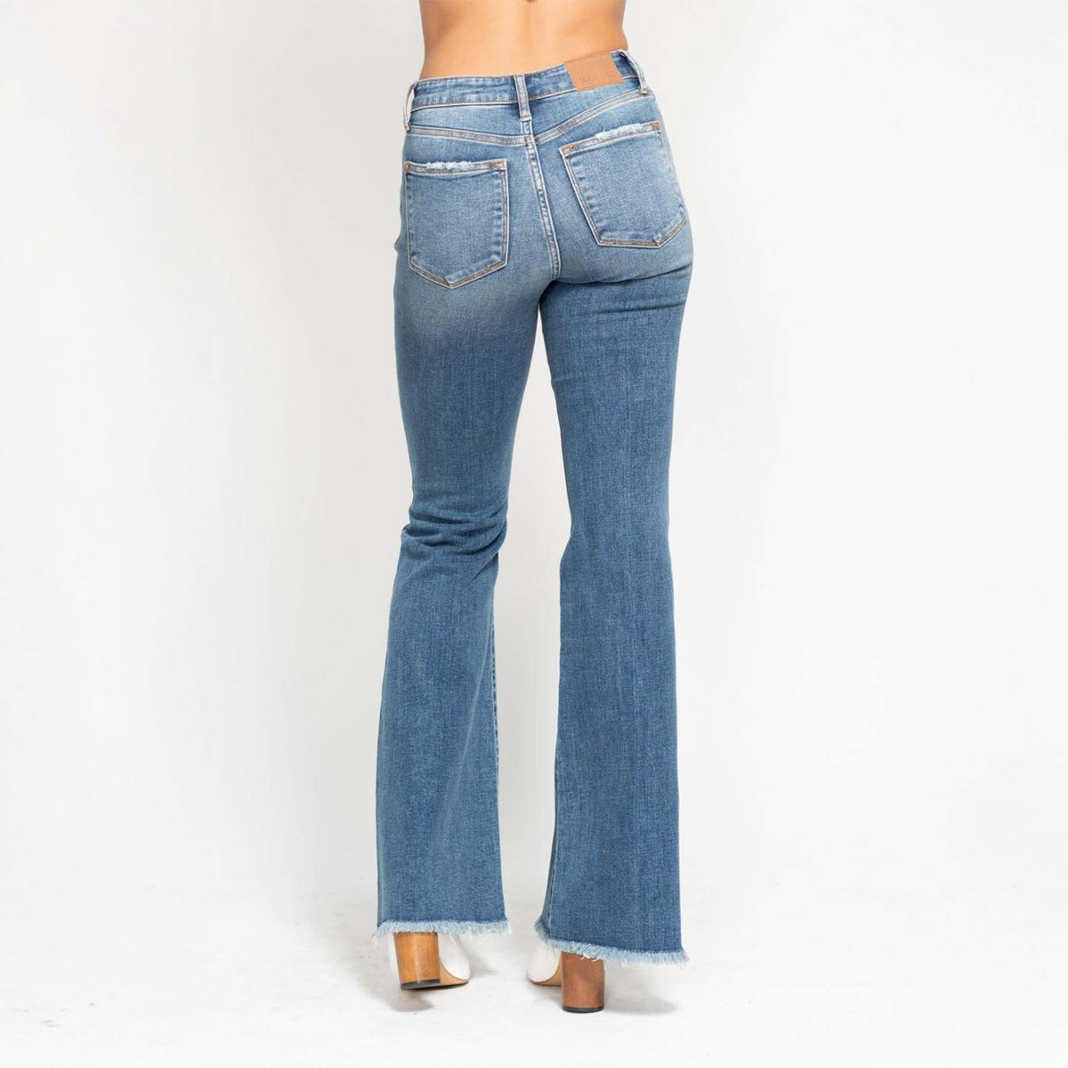 Back view of Judy Blue medium wash flare jeans, showing classic back pockets and flared leg with frayed hem detail.