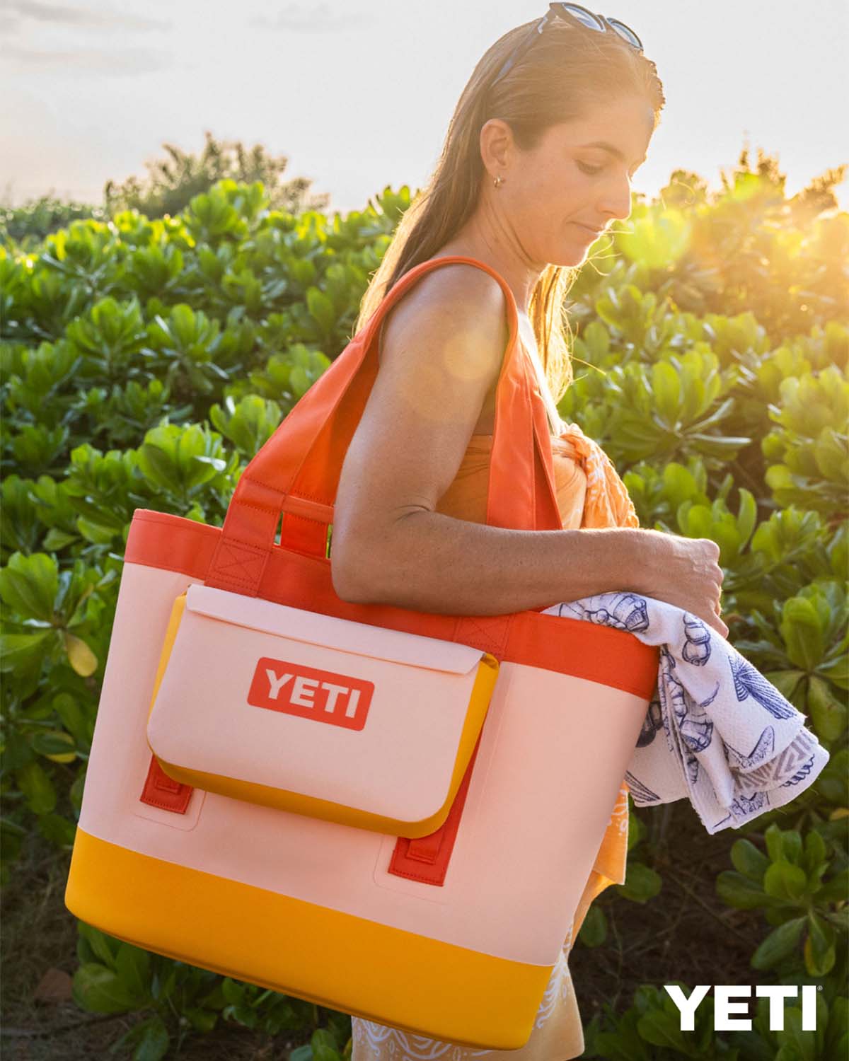 Woman holding a YETI Camino bag on her shoulder that is colorblock peach, orange, and yellow.