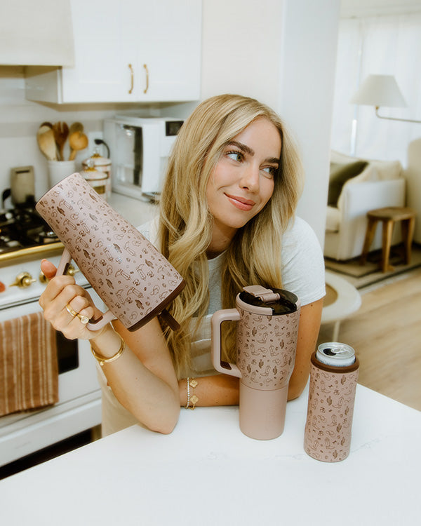 girl standing in her kitchen posing for a picture with her brumate tumbler line