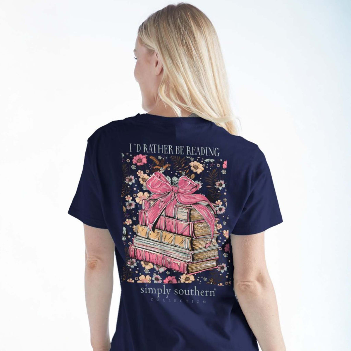 Back view - Woman wearing the Simply Southern short sleeve t-shirt, color navy, sizes S-XXL, 100% cotton.  This shirt features a large design of pink stacked books with a pink bow on top and the words &quot;I&#39;d rather be reading&quot; on top of the design and the Simply Southern Logo at the bottom.  