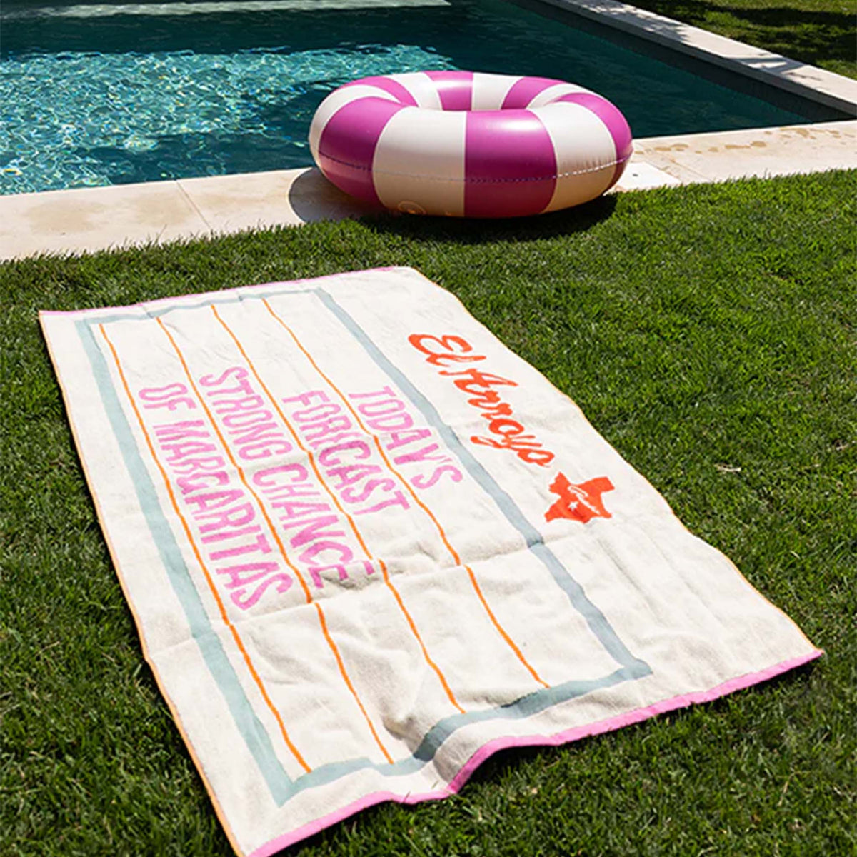 Outdoor, poolside view - Oversized beach towel, size 36 inches by 70 inches, color ivory.  The design is a green outlined marquee style sign featuring the humorous phrase &quot;Today&#39;s forecast: Strong Chance of Margaritas&quot; typed in pink font. 